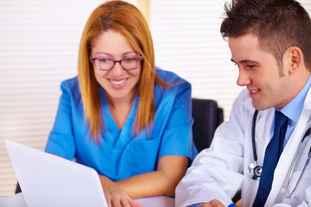 Portrait of a young doctor and a nurse talking and using a laptop on the office.の写真素材