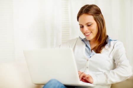 Portrait of a cute young woman smiling and working on laptop at homeの写真素材