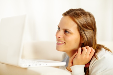 Close up portrait of a young lovely woman lying on sofa and looking to laptop screen while restingの写真素材