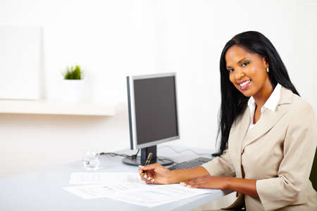 Portrait of a young professional woman on work desk, smiling and looking to you whole working on documentsの写真素材