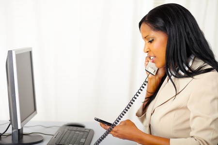 Portrait of a young professional woman talking on phone while use a mobile phone at workの写真素材