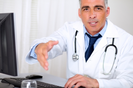 Portrait of a senior trustworthy doctor in from the computer while greeting and looking to youの写真素材