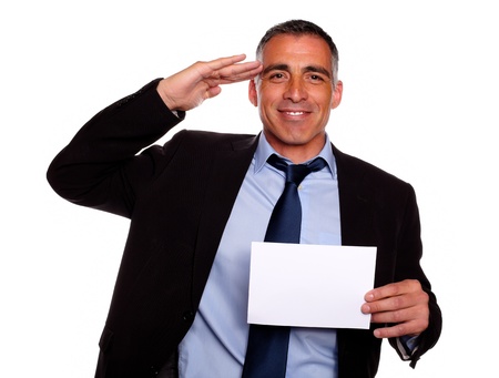 Portrait of a friendly senior businessman giving a military salute, smiling and holding a white card with copyspace against white backgroundの写真素材