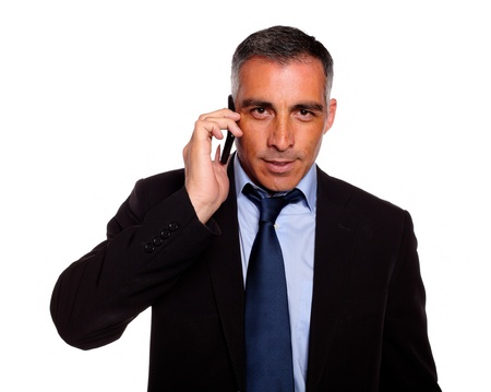 Portrait of a hispanic professional businessman conversing with a mobile looking to you against white backgroundの写真素材