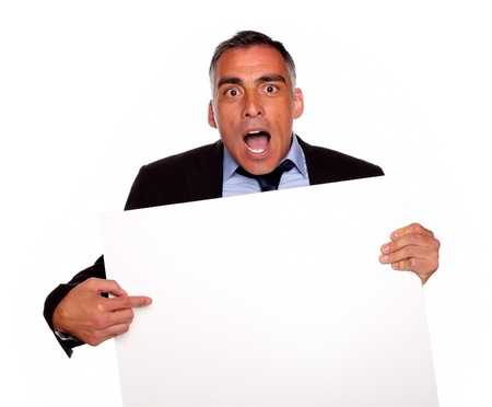 Portrait of a surprised businessman pointing and holding a white card with copyspace on isolated backgroundの写真素材