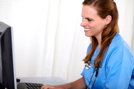 Portrait of a blonde friendly nurse  looking to computer screen at workplaceの写真素材