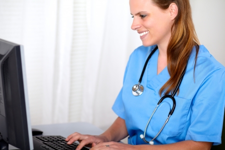 Portrait of a blonde friendly young nurse looking to computer screen at hospitalの写真素材