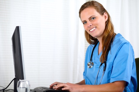 Portrait of a beautiful friendly nurse smiling while working on computer at workplaceの写真素材