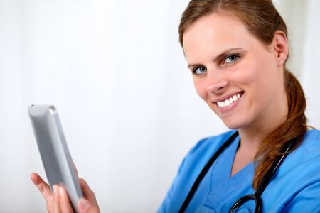 Close up portrait of a beautiful blonde nurse smiling with a tablet PC at hospitalの写真素材