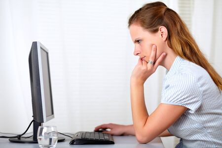 Portrait of a beautiful caucasian blonde woman reading on computer at home indoorの写真素材