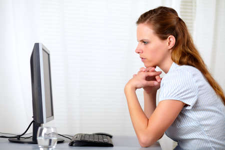 Portrait of a blonde friendly young woman looking to screen monitor at office indoorの写真素材