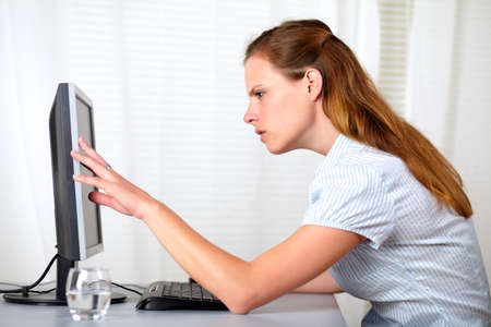 Portrait of a blonde young woman looking and pointing to screen monitor at workplace indoorの写真素材