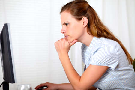 Portrait of a charming pensive pretty girl looking on computer at workplace indoorの写真素材