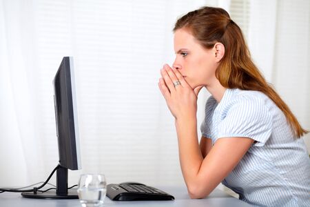 Portrait of a blonde friendly young reflective lady looking to computer at office indoorの写真素材