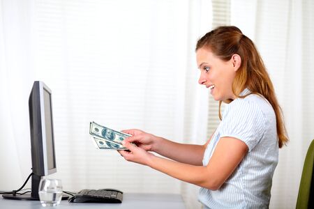 Portrait of a surprised beautiful woman looking and holding dollars at officeの写真素材