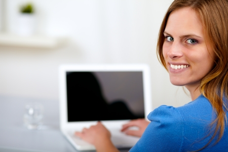 Portrait of a young woman working on laptop on blue shirt at home indoorの写真素材