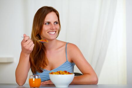 Portrait of a beautiful blonde young woman eating cereals and strawberry for breakfast at homeの写真素材