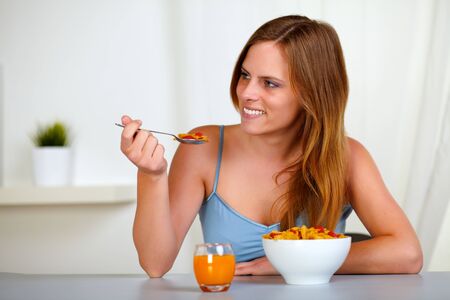 Portrait of a pretty lovely woman smiling and eating cereals and strawberry for breakfast at home