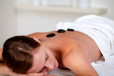 Close up portrait of a young woman relaxing face down having hot stones placed in a row down her back at a health spaの写真素材