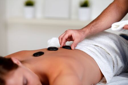 Close up portrait of a tired woman relaxing at a spa and receiving a hot stone massageの写真素材