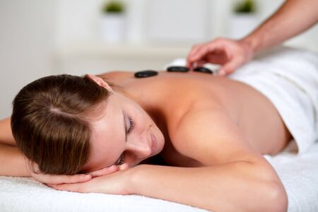 Close up portrait of a tired young female relaxing at a spa and receiving a hot stone massageの写真素材