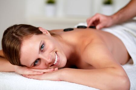 Close up portrait of a relaxed woman receiving a hot stone massage at spa, looking at youの写真素材