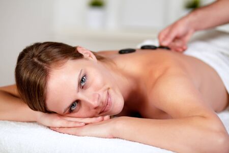 Close up portrait of a relaxed female receiving a hot stone massage at spa, looking at youの写真素材