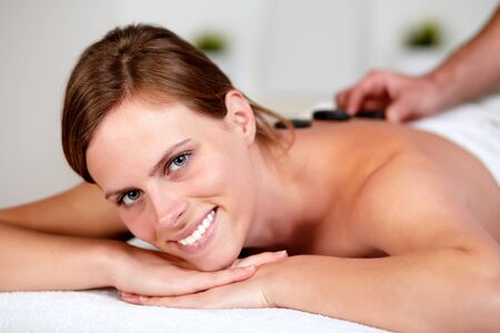 Close up portrait of a relaxed girl receiving a hot stone massage at spa, looking at youの写真素材