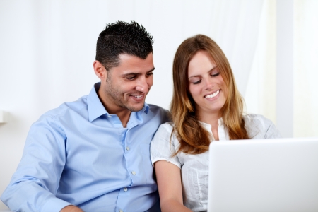 Portrait of a friendly couple using a laptop at home indoorの写真素材