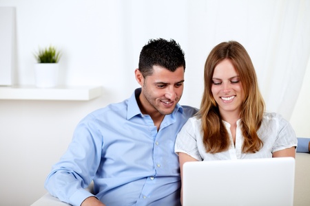 Portrait of a young couple smiling and using a laptop at home indoorの写真素材