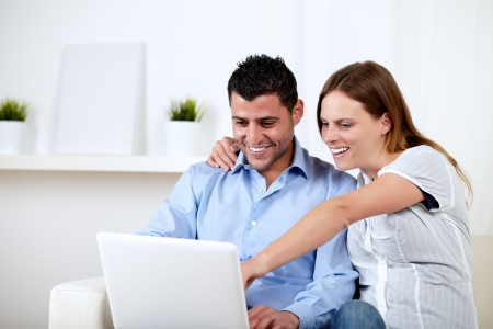 Portrait of a young couple smiling and pointing to laptop screen at home indoorの写真素材