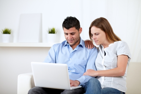 Portrait of a young man with his girlfriend chatting on laptop at home indoorの写真素材