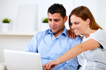 Portrait of a charming young couple sitting on sofa using laptop at home indoorの写真素材