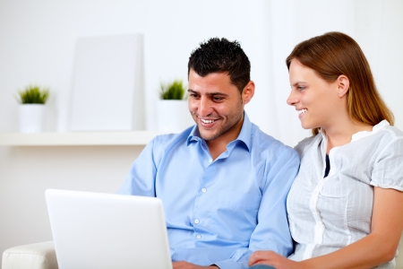 Portrait of a happy young couple sitting on sofa and working on laptop at homeの写真素材