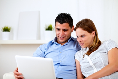 Portrait of a beautiful young couple using laptop together at home indoorの写真素材