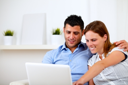 Portrait of a friendly young couple using laptop together at home indoorの写真素材