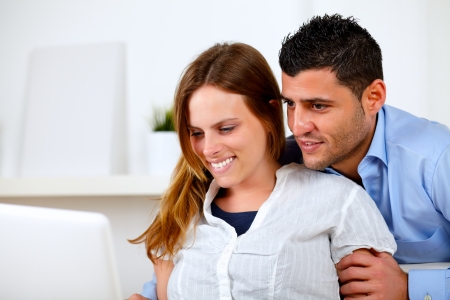 Portrait of a charming young couple browsing Internet together on their laptop at home indoorの写真素材