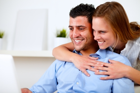 Portrait of a charming young couple browsing Internet together on their laptop at living room at home indoorの写真素材