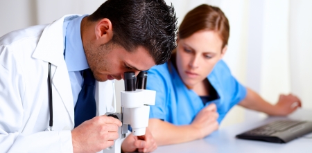 Portrait of a handsome professional medical using a microscope with a pretty nurse at hospitalの写真素材