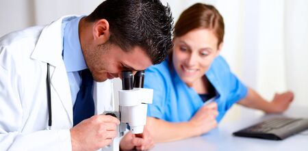 Portrait of a handsome medical doctor using a microscope with a pretty and happy nurse at hospitalの写真素材