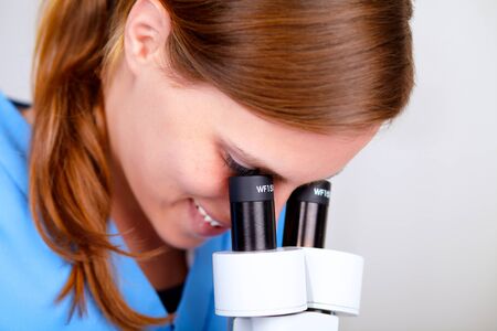 Closeup portrait of a young beautiful nurse working with a microscope at laboratory indoorの写真素材