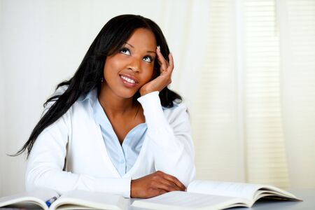 Portrait of a beautiful tired black student woman thinking while is looking up at home indoorの写真素材