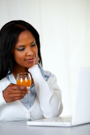 Portrait of an afro-American young woman drinking orange juice while looking to laptop screenの写真素材