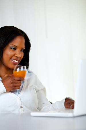 Portrait of a lovely student girl smiling and looking to laptop screen while drinking a healthy orange juice at soft colors compositionの写真素材
