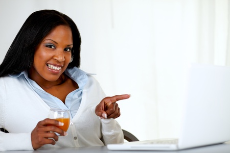 Portrait of a beautiful afro-american woman pointing the laptop screen at soft colors compositionの写真素材