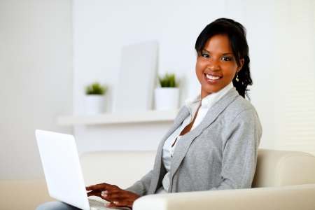 Portrait of a happy woman browse the Internet on laptop while is sitting on sofa at homeの写真素材