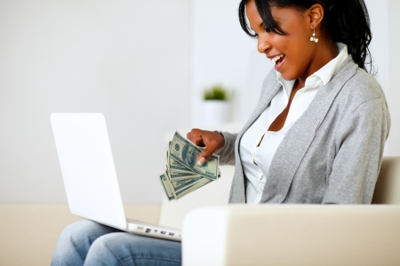 Portrait of a surprised woman with dollars looking to laptopの写真素材