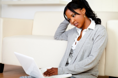 Portrait of a beautiful young woman working relaxed on laptop while is sitting on the floor at homeの写真素材