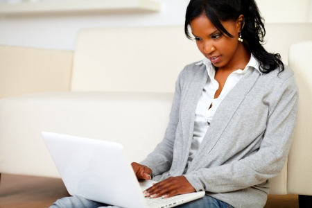Portrait of an afro-American young female sitting at home on the floor using her laptopの写真素材