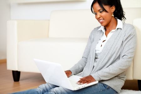 Portrait of a young girl smiling and browsing the Internet at home with her laptop while is sitting on the floorの写真素材